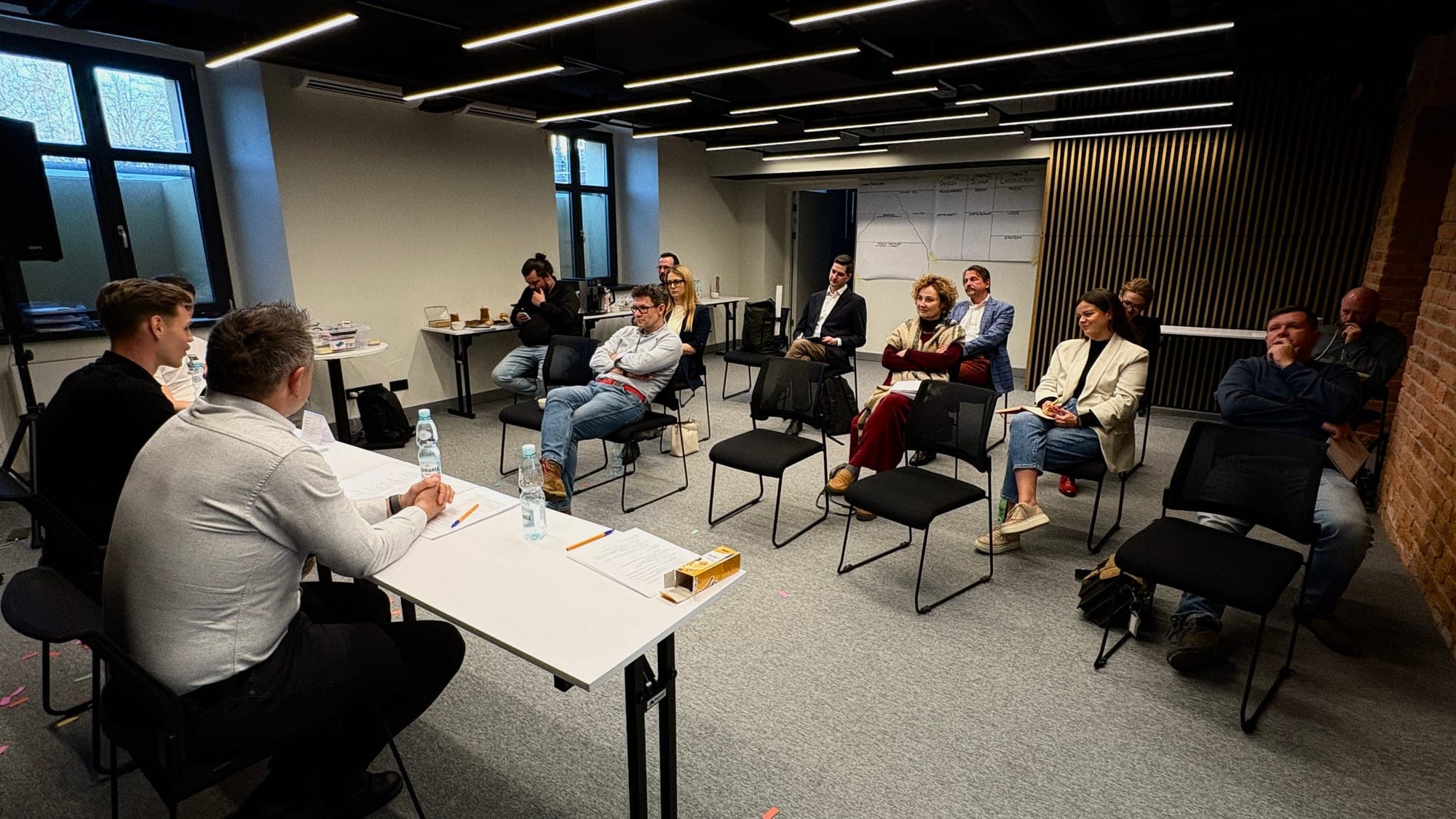Uczestnicy pierwszej edycji POST-CI LAB siedzą w kręgu, w tle widoczna ściana Master Mapy